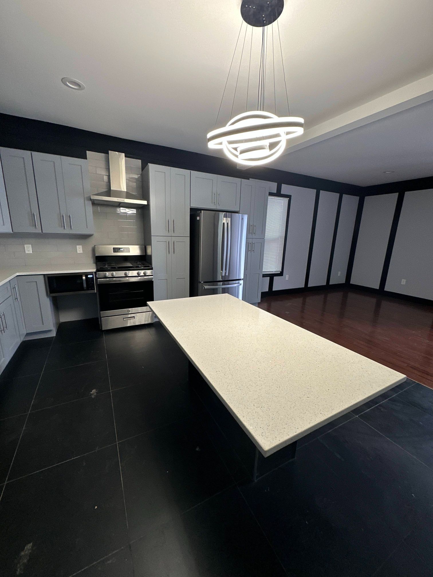 Modern kitchen with gray cabinets, stainless steel appliances, large island, and unique light fixture.