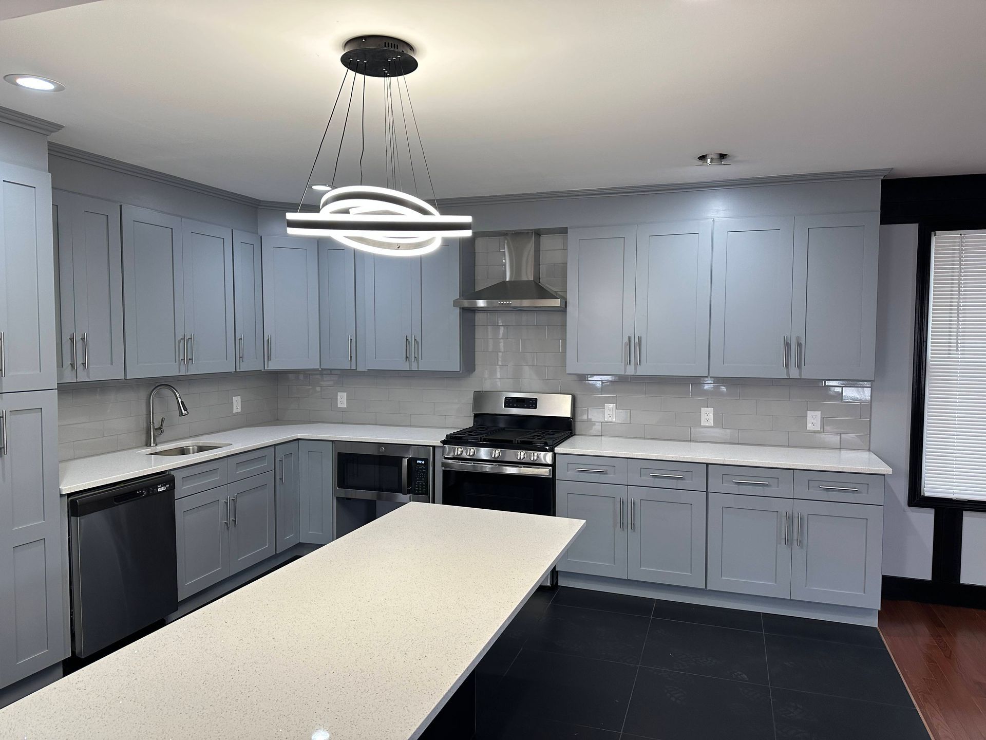 Modern kitchen with gray cabinets, white countertops, and stainless steel appliances.