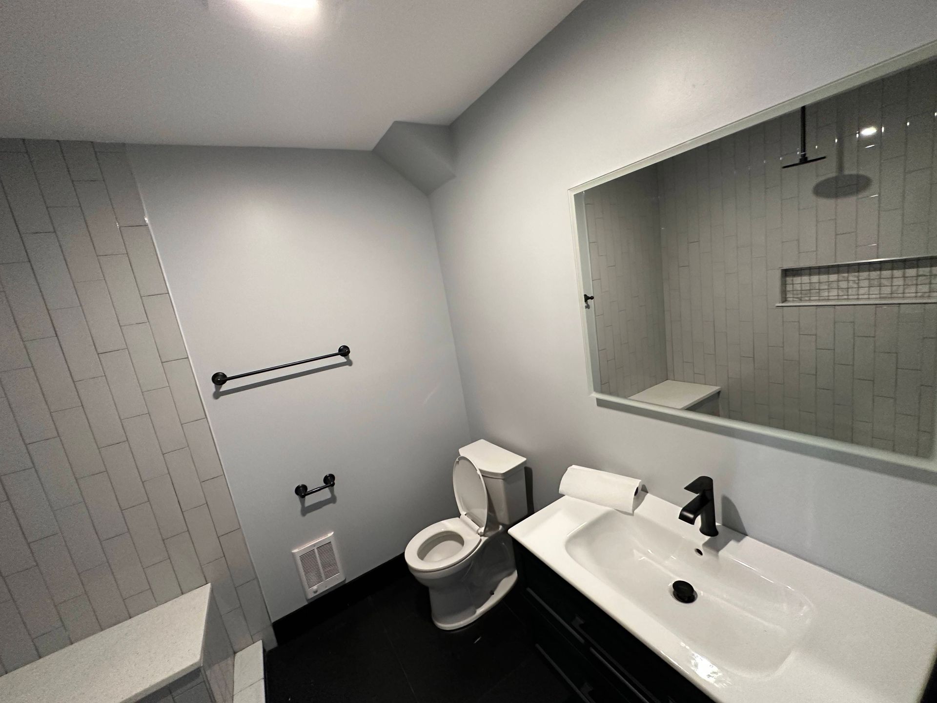 Bathroom with gray walls, black floor, white sink, toilet, and shower.