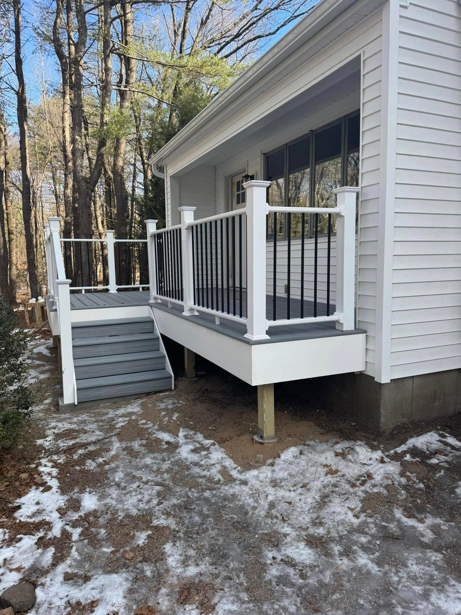 Deck with gray steps, white railing and black spindles, attached to a white house.