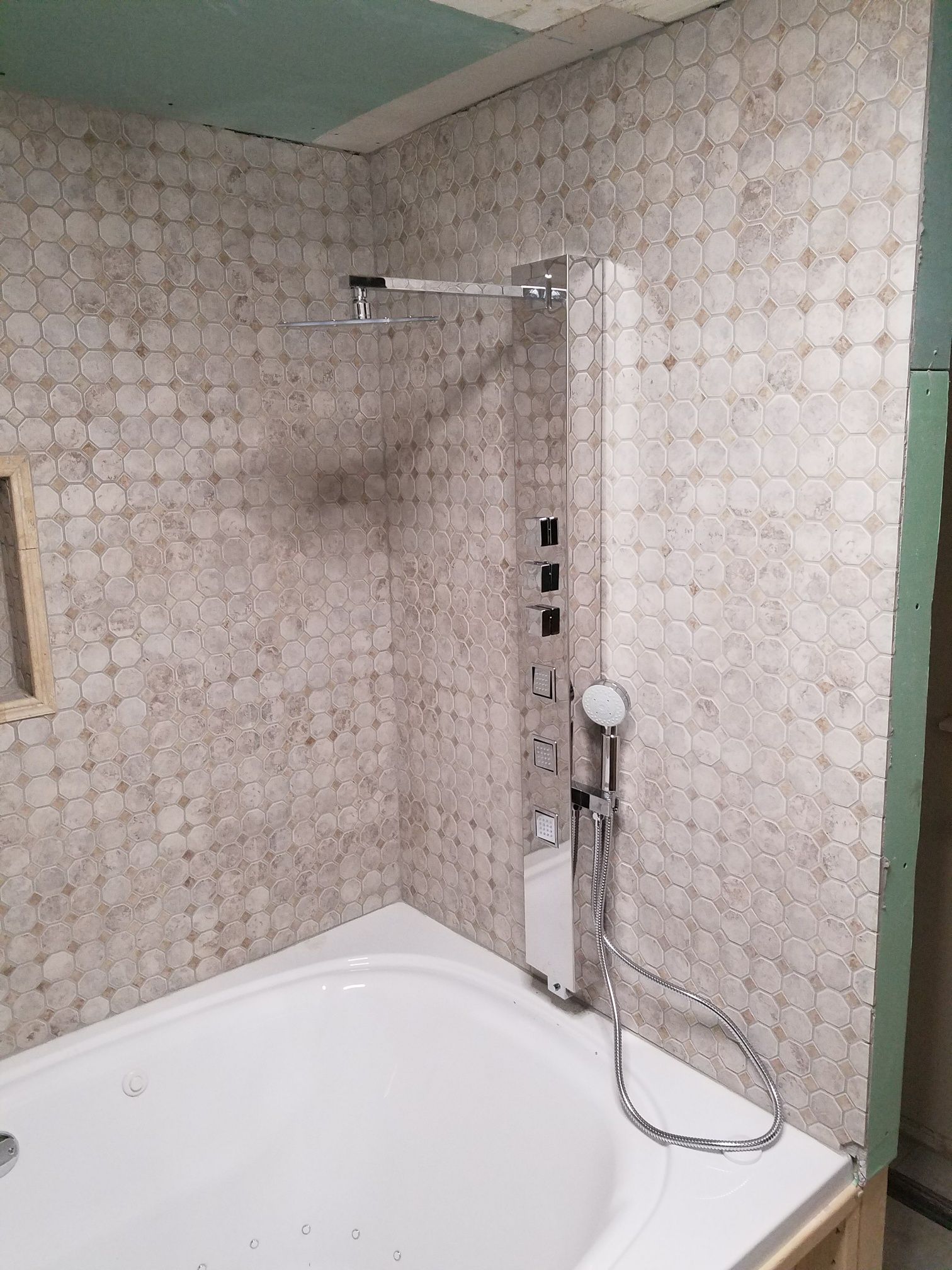 Shower unit with multiple showerheads, installed on a tiled wall above a white bathtub.