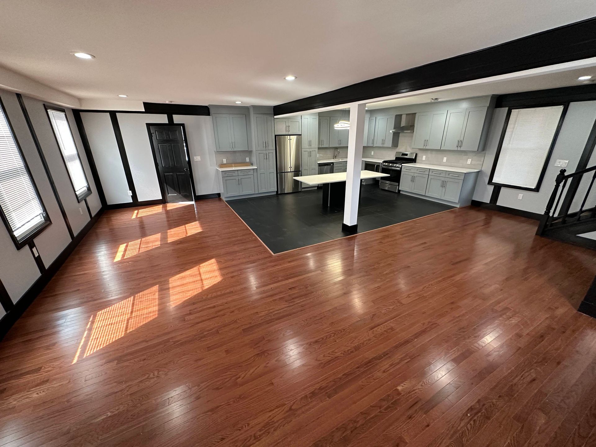 Spacious open-concept living space with hardwood floors, kitchen area, and dark accents.