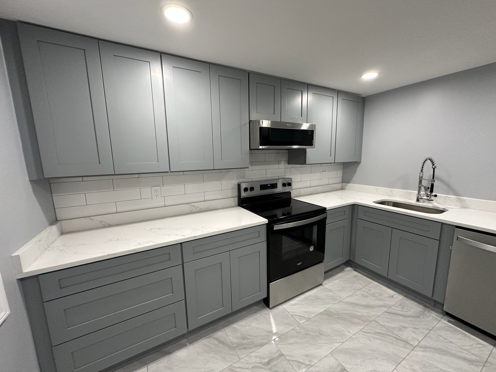 Gray kitchen cabinets with white countertops, stainless steel appliances, and gray tiled floor.