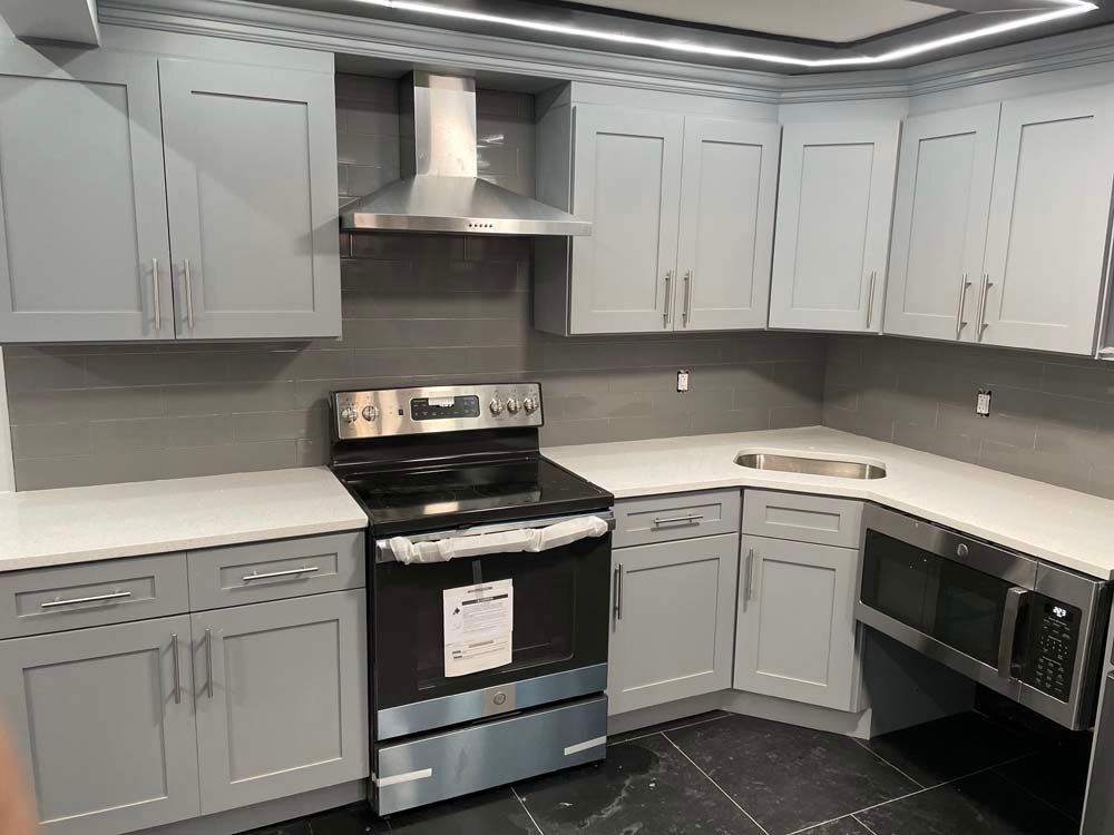 Gray kitchen cabinets with white countertops, stainless steel appliances, and gray backsplash.
