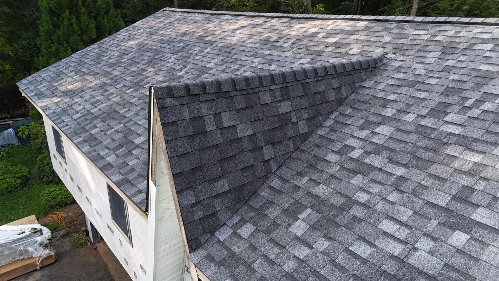 Gray asphalt shingle roof on a two-story white house with surrounding green trees.