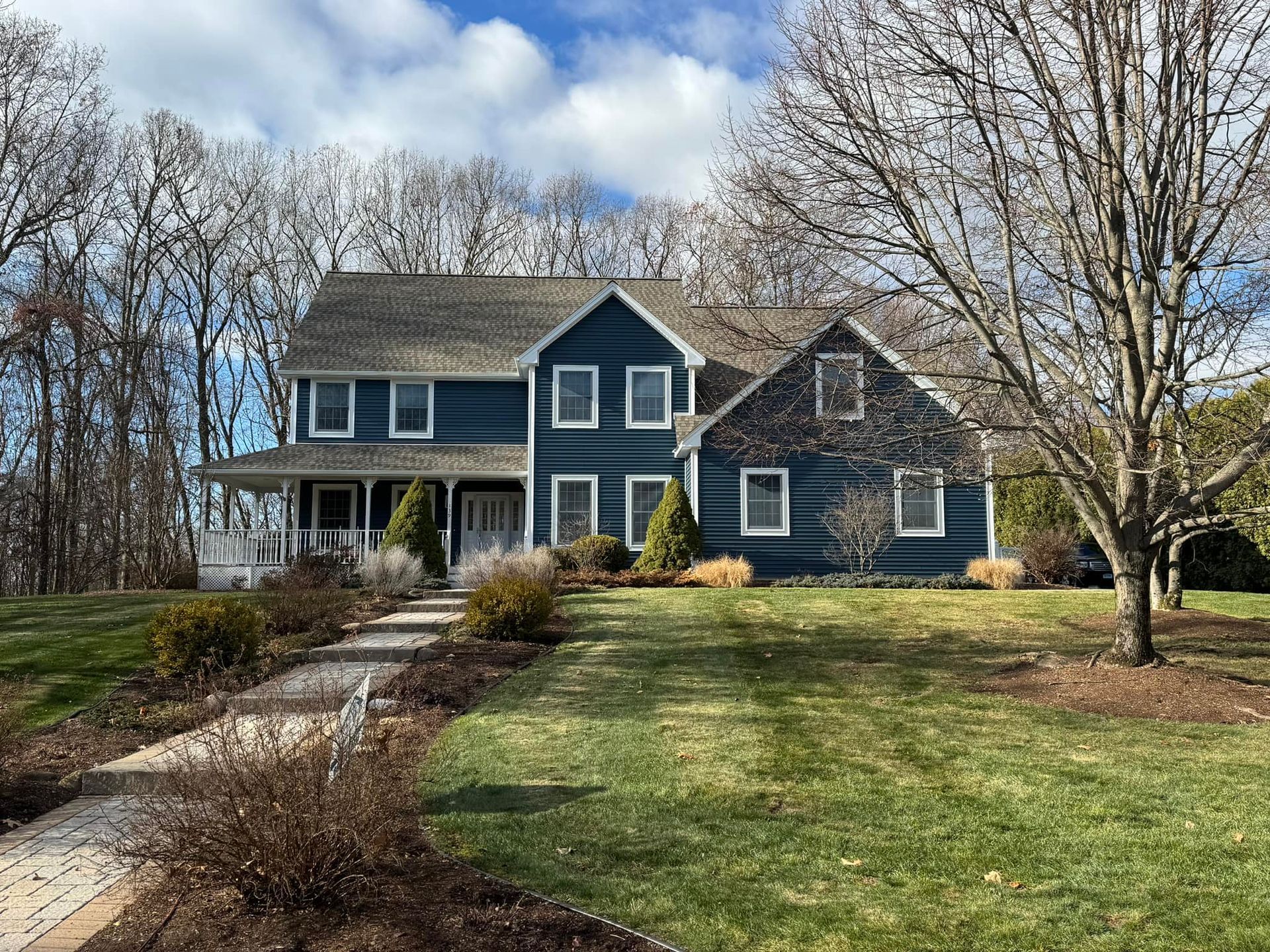 Two-story blue house with porch, walkway, and trees. Overcast sky.
