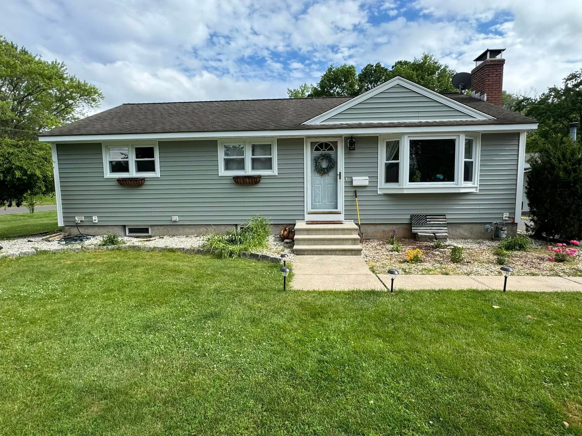 Cottage-style house with green siding, a small front porch, and a green lawn under a cloudy sky.