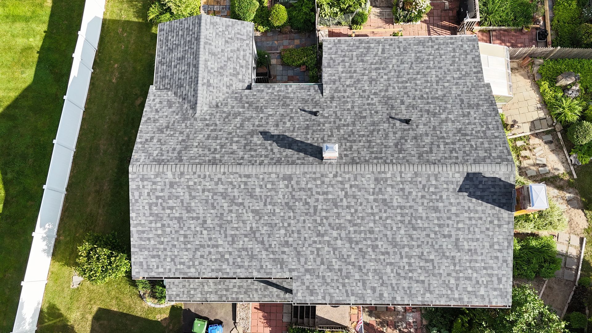 Overhead view of a house with a gray shingle roof, chimney, and surrounding greenery.