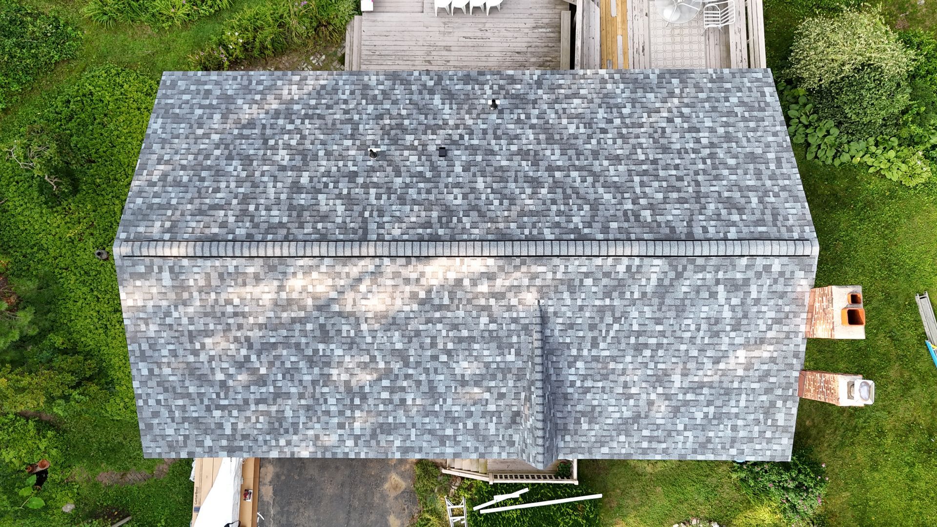 Overhead view of a house with a gray shingled roof surrounded by green grass.