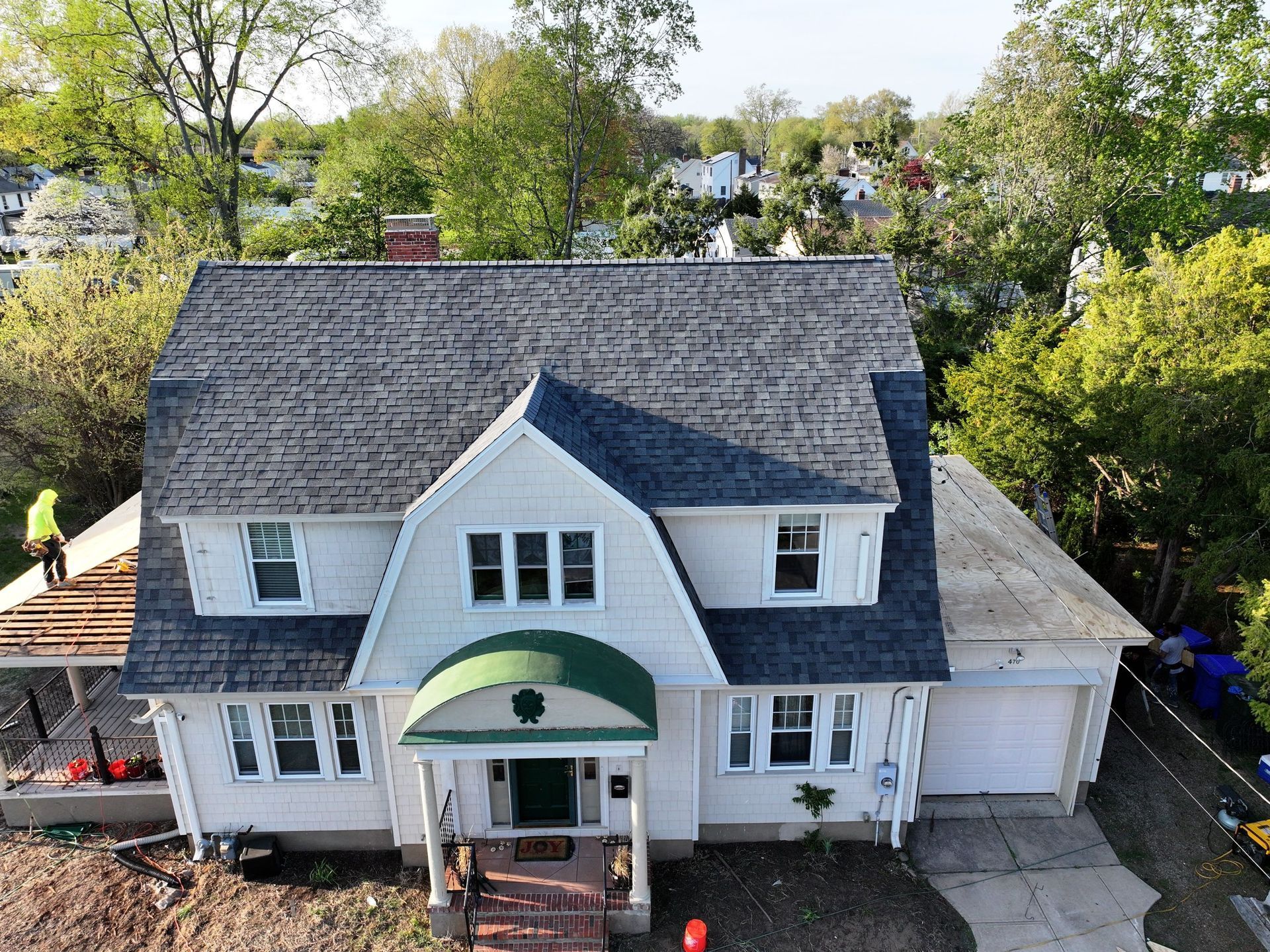 Aerial view of a white house with a new dark gray roof; construction worker on the porch roof.