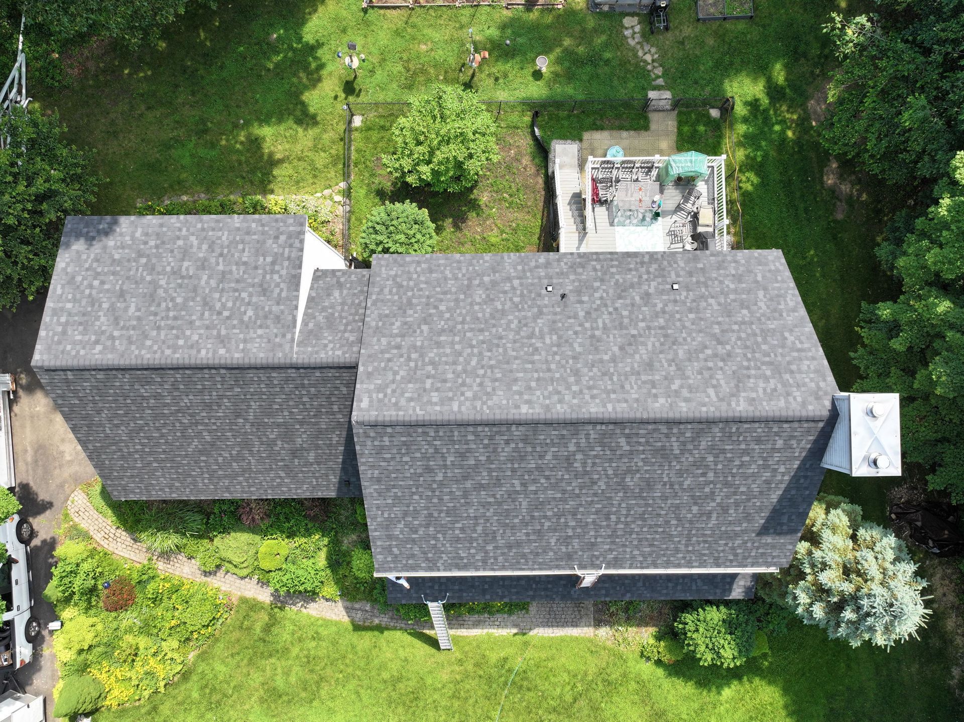 Overhead view of a house with a dark gray roof surrounded by green grass and trees.