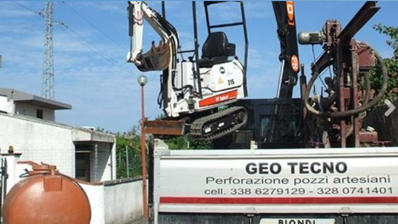 A white mini excavator mounted on a flatbed truck for a drilling company with contact info displayed on the side.