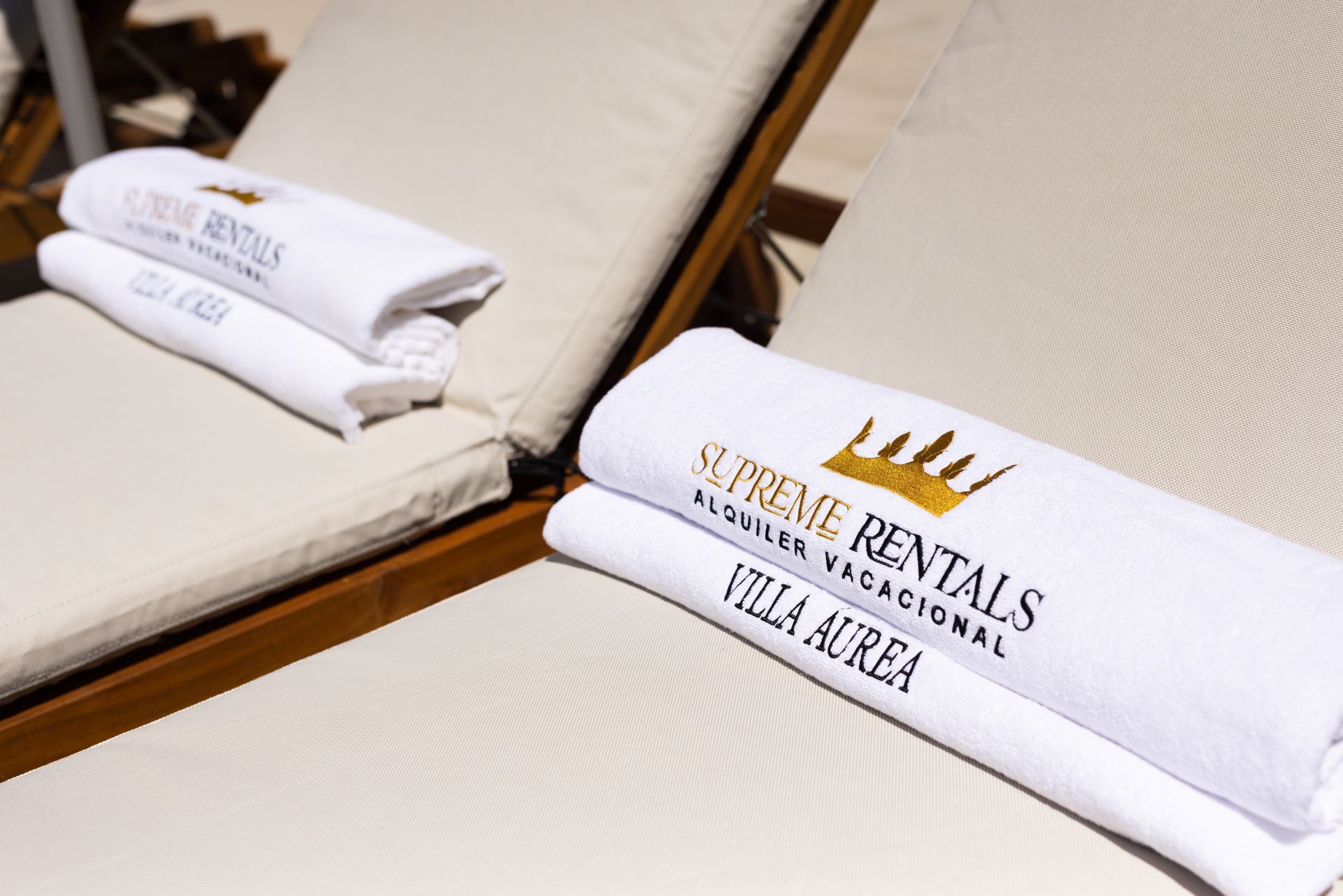 Toallas blancas dobladas sobre tumbonas beige con bordado “Villa del Mar” y logotipo del sol.
