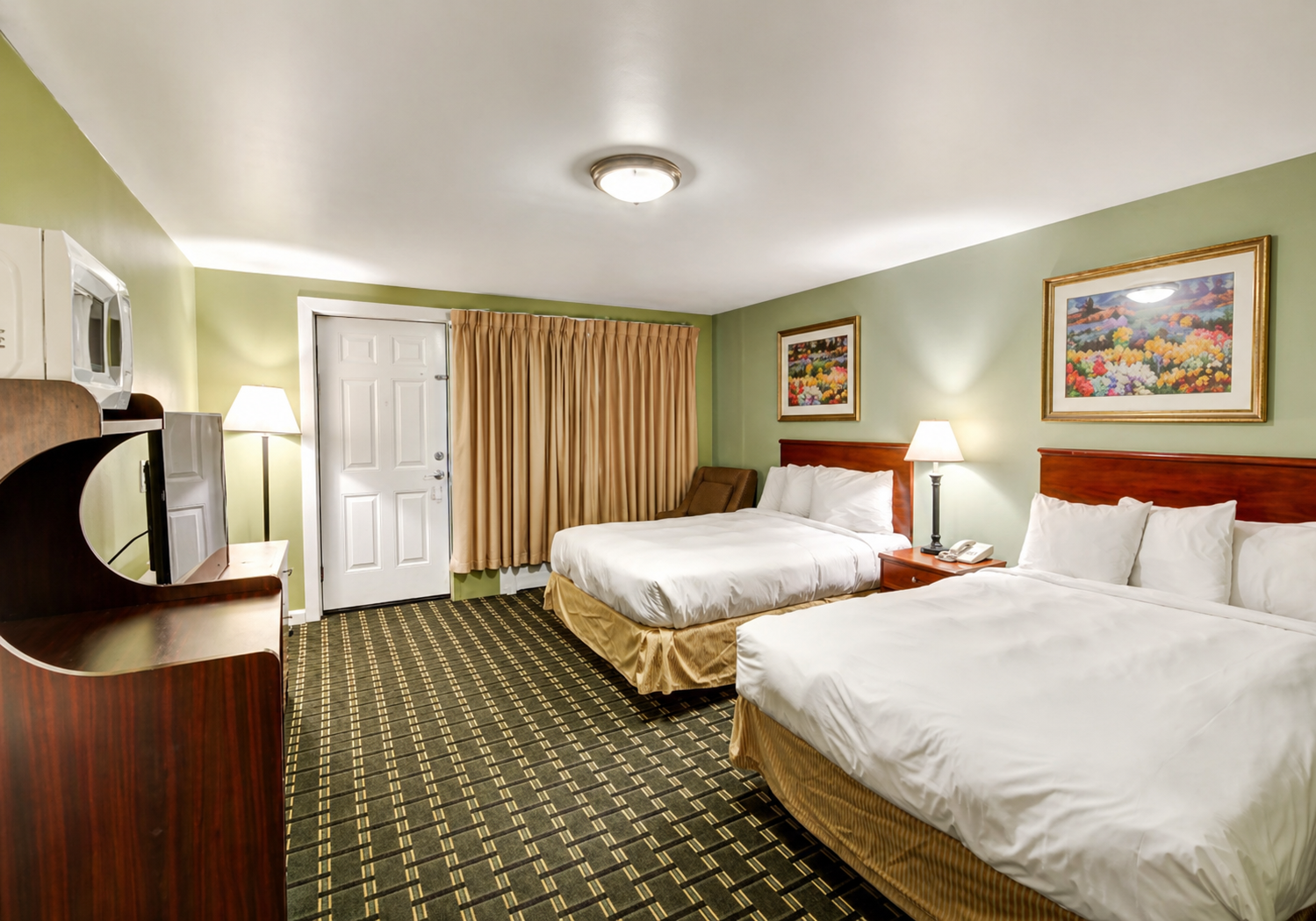 Hotel room with two beds, white linens, beige curtains, and framed artwork on light green walls