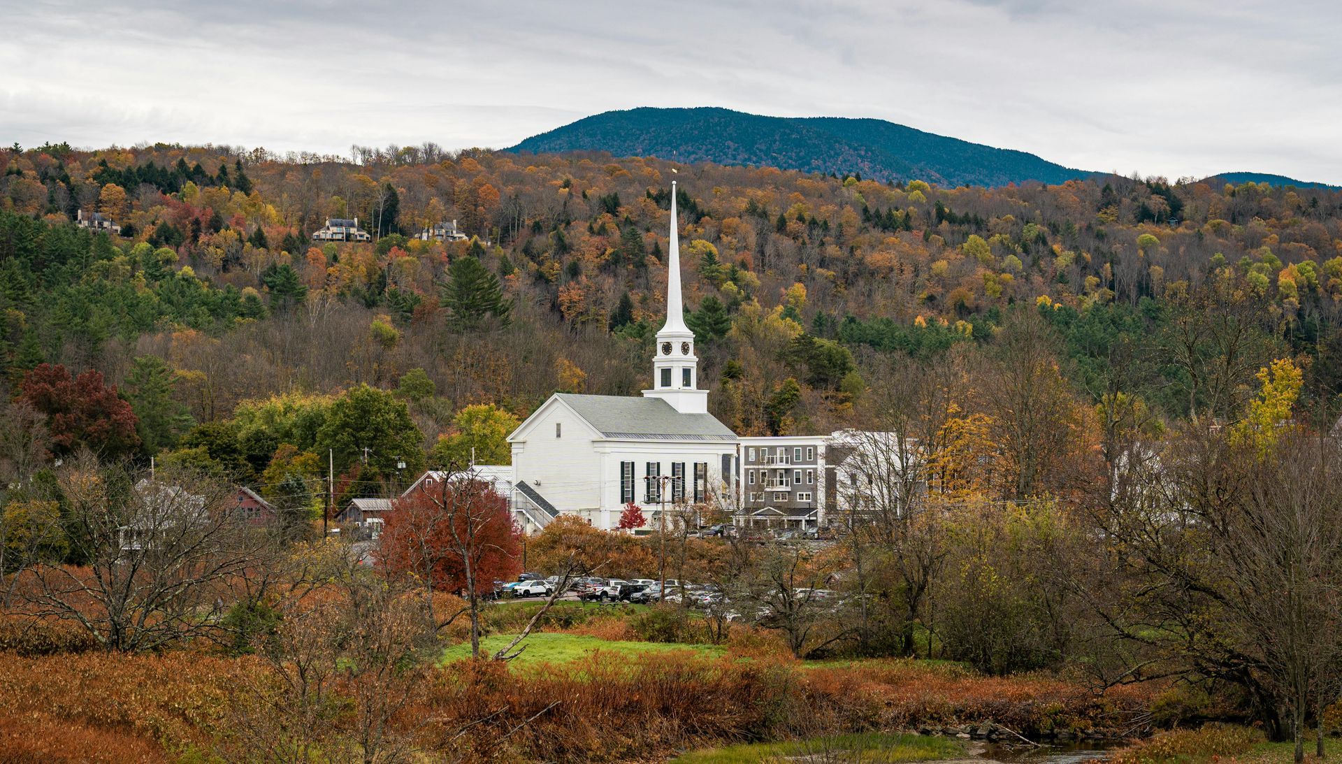 White church with steeple amid autumn trees, with a mountain in the background.