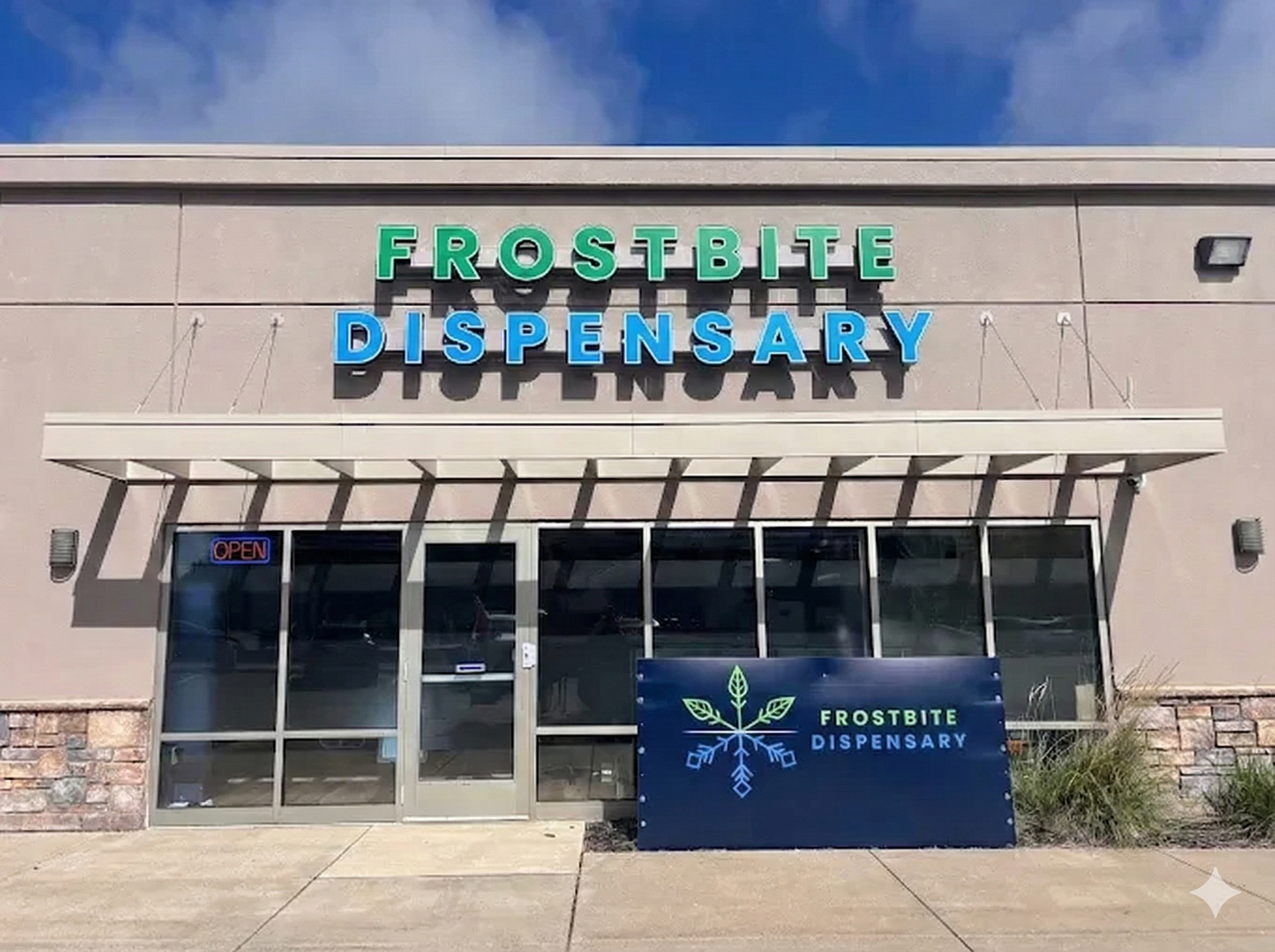 Frostbite Dispensary storefront with teal and green sign, blue sign below, against a blue sky.