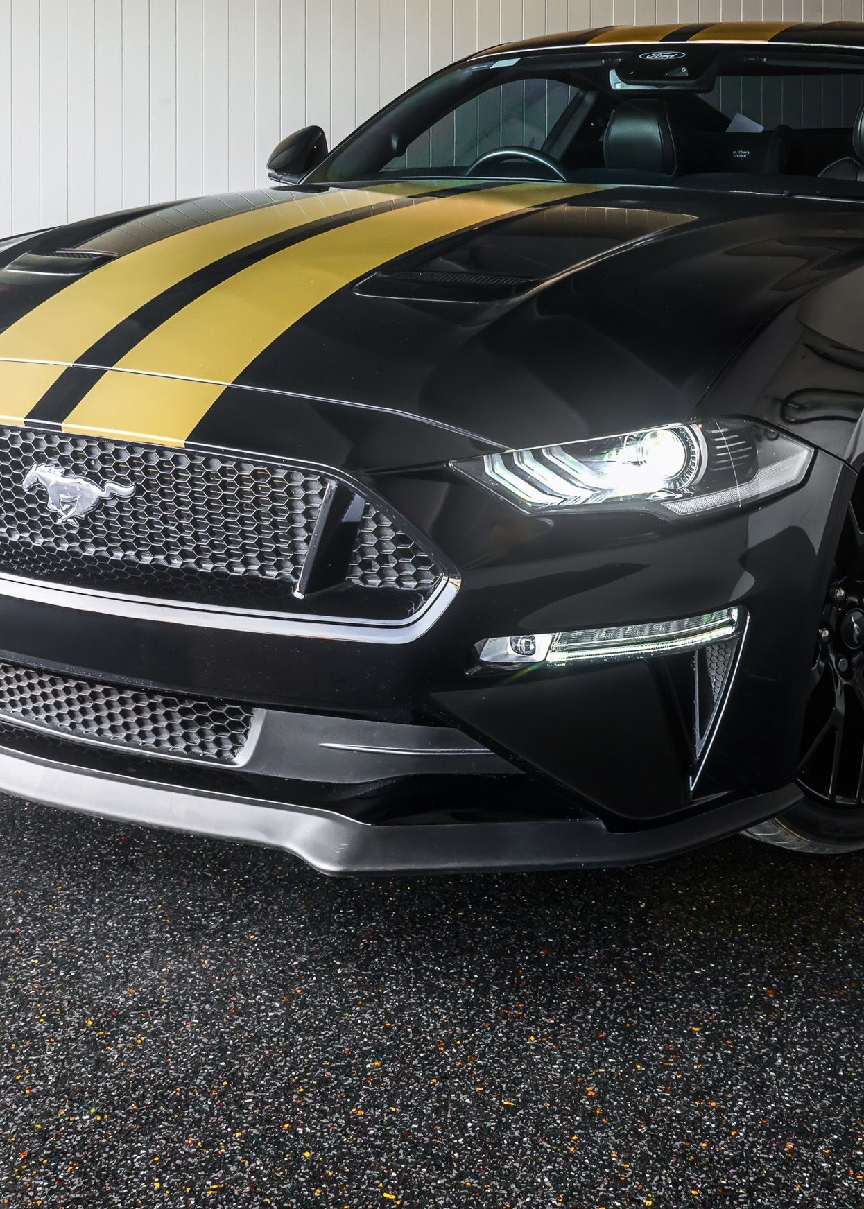 A black mustang with yellow stripes on the hood