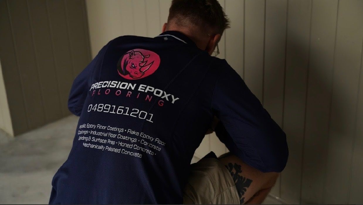 A man wearing a blue shirt that says precision epoxy flooring