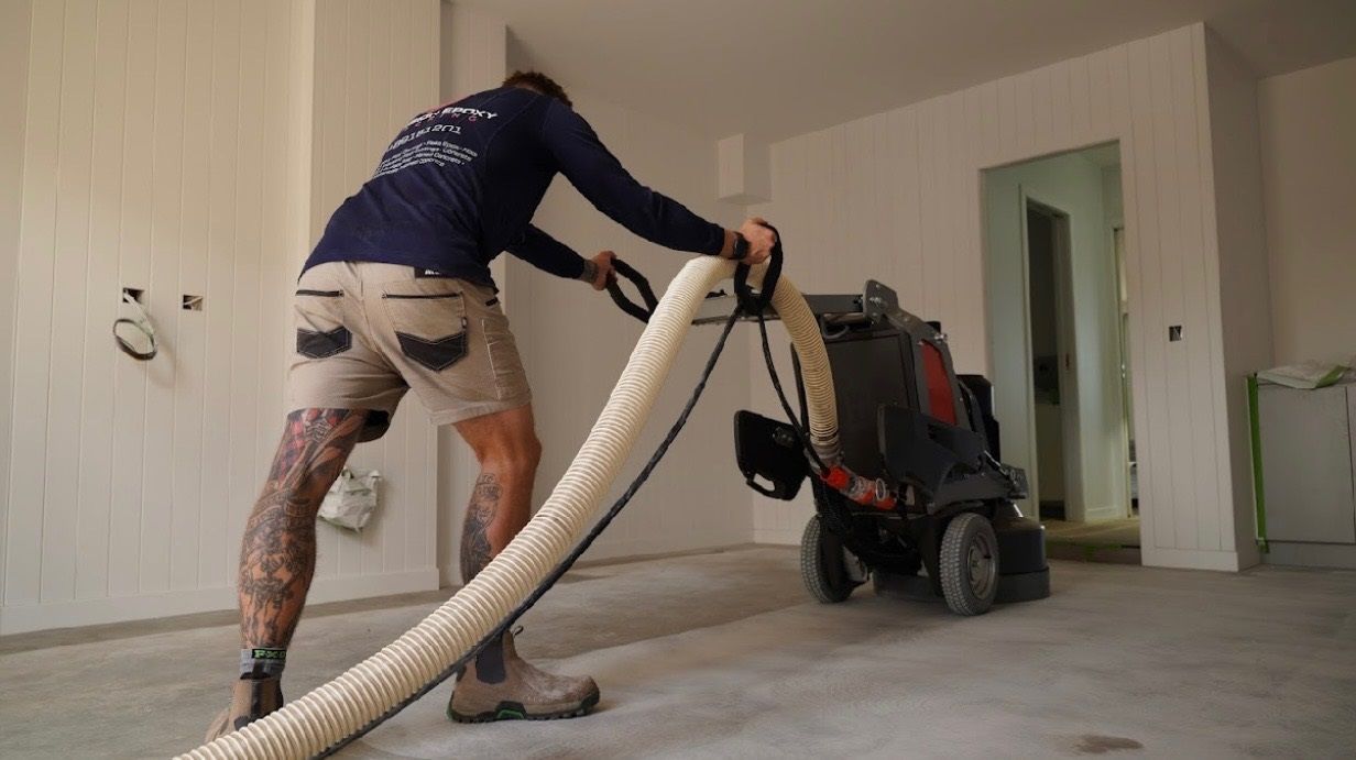 A man is using a vacuum cleaner to clean a concrete floor.