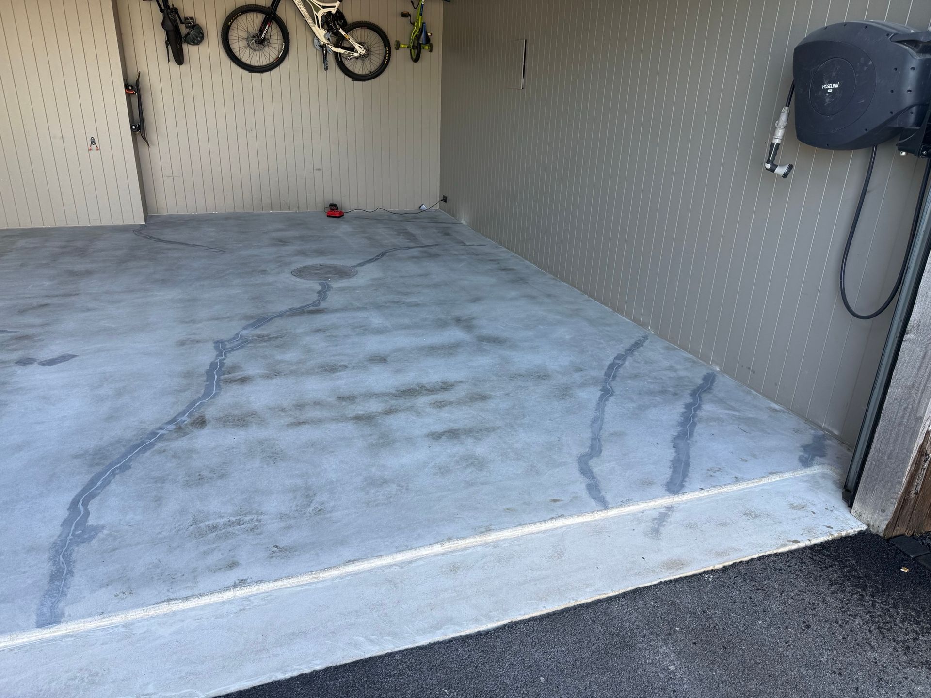 A concrete floor in a garage with bikes hanging on the wall.