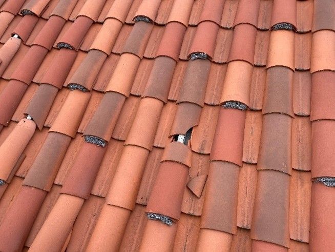 Roofer in blue shirt and jeans working on a terracotta tile roof under a cloudy sky.