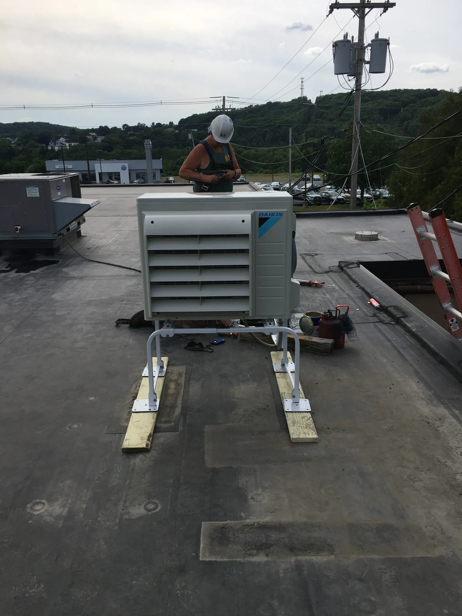A man is working on a rooftop air conditioner.