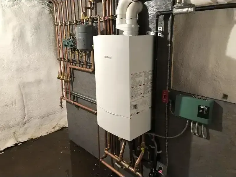 A white boiler is sitting in a basement next to copper pipes.