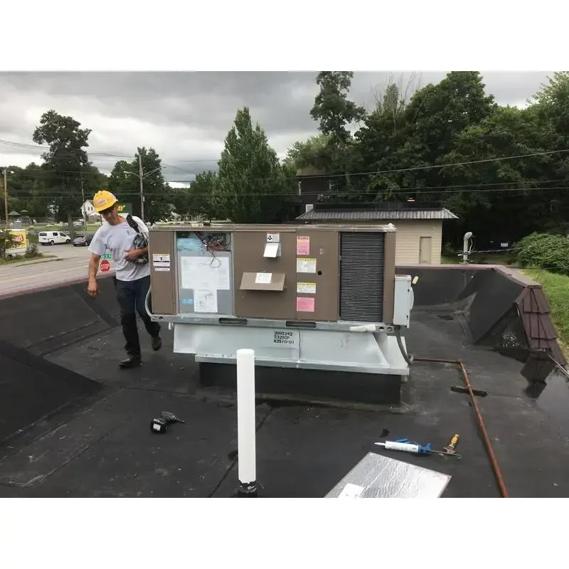 A man is standing next to a large air conditioner on a roof.