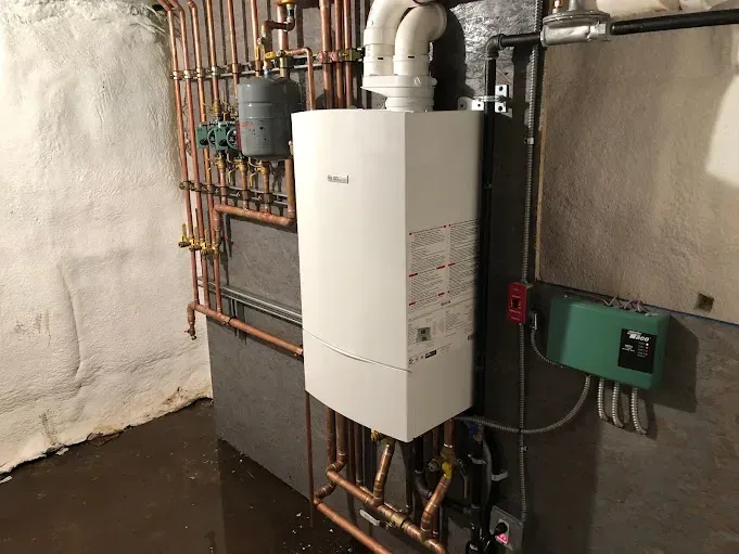 A white boiler is sitting in a basement next to copper pipes.