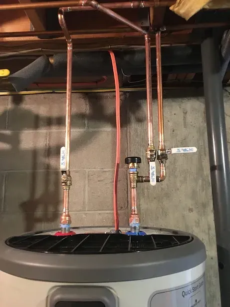 A water heater is being installed in a basement with copper pipes hanging from the ceiling.