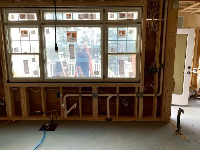 A man is standing in front of a window in a room under construction.