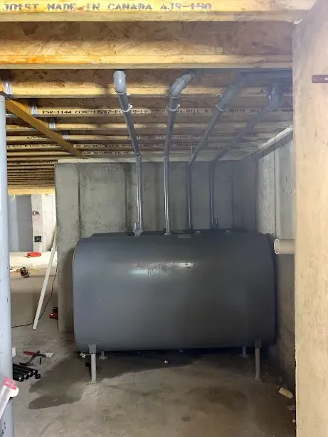 A large gray tank is sitting in a basement under a wooden ceiling.