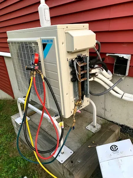 A daikin air conditioner is being serviced outside of a house