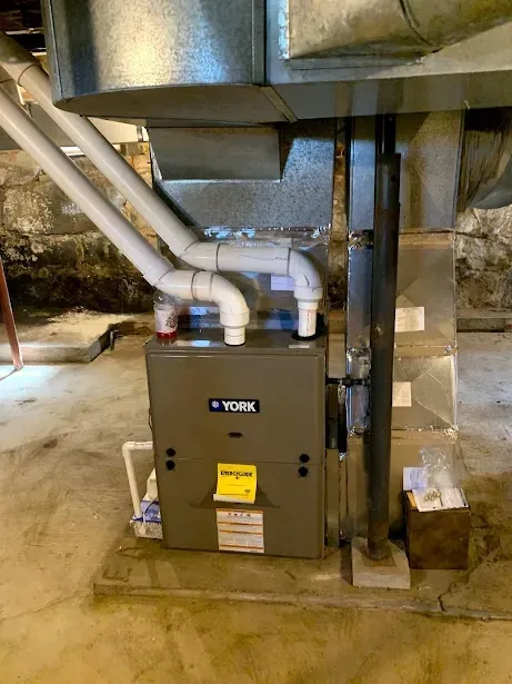 A york furnace is sitting in a basement next to a pipe.