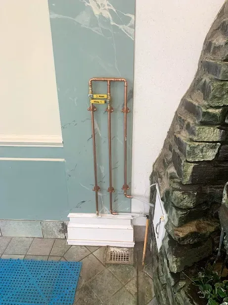 A copper pipe is attached to a wall next to a stone wall.