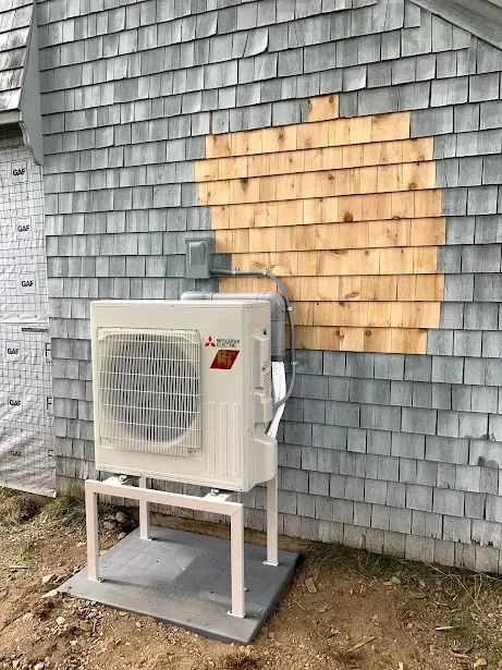 A white air conditioner is sitting on the side of a brick building.