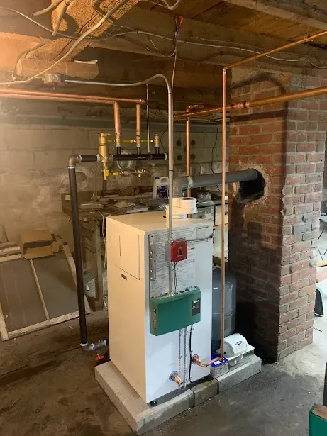 A boiler is sitting in a basement next to a brick wall.