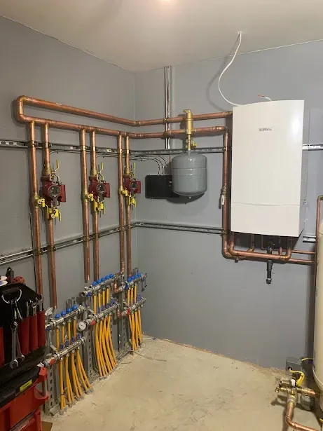 A room with a boiler and copper pipes on the wall.