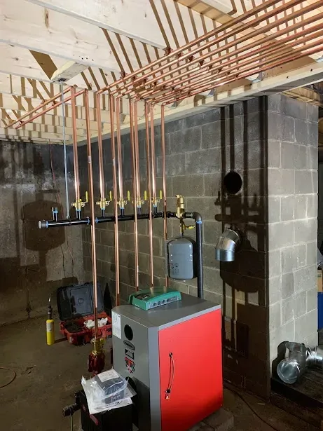 A boiler is being installed in a basement with copper pipes hanging from the ceiling.