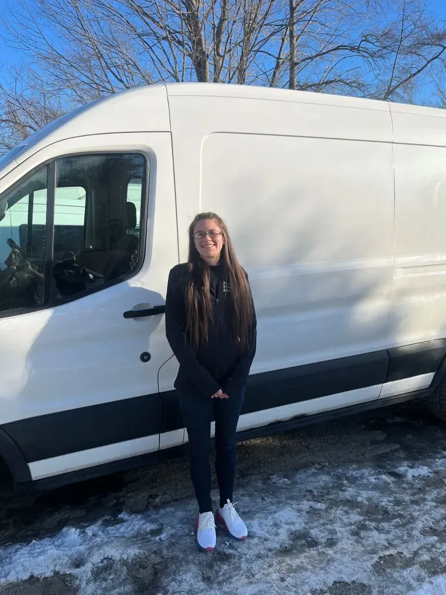 A woman is standing in front of a white van in the snow.