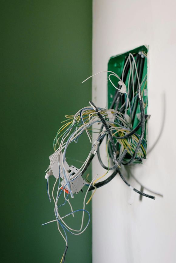 Electrical wires spilling out of a wall-mounted green junction box on a corner.