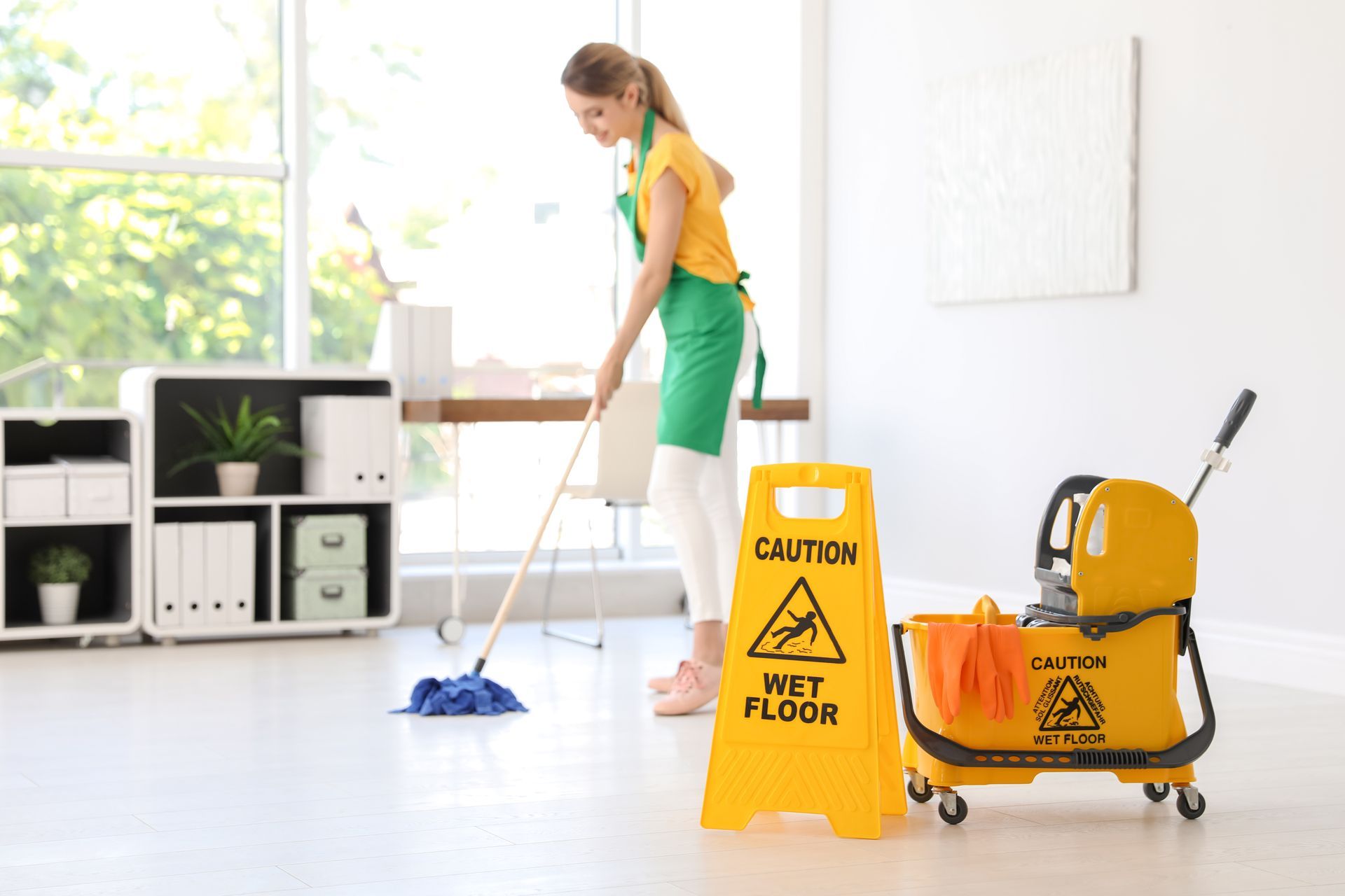 The janitorial staff mops the bright office; caution signs and buckets highlight safety.