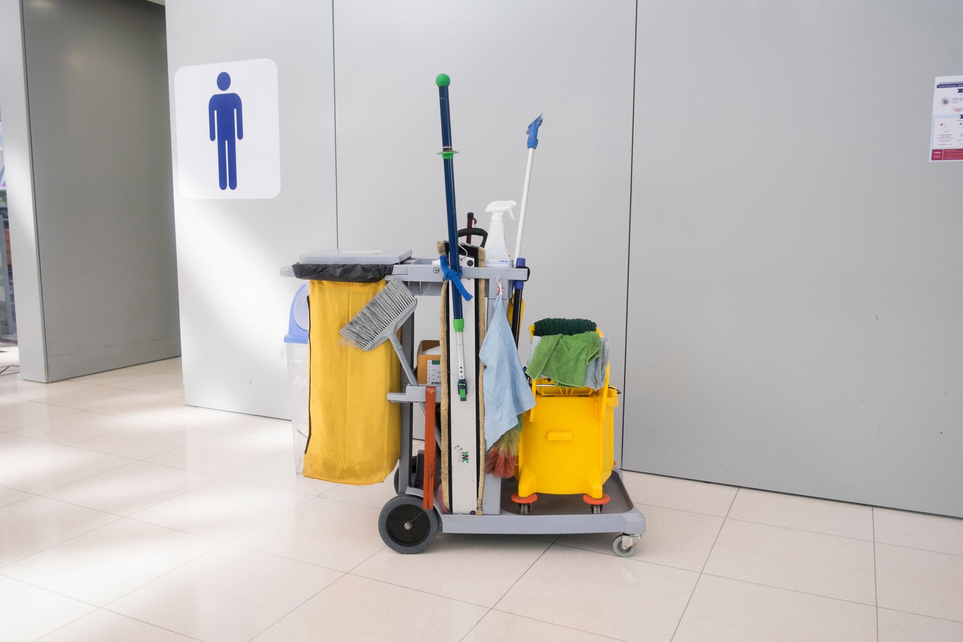Cleaning cart with tools, cleaning buckets and cleaning equipment standing near restroom door.