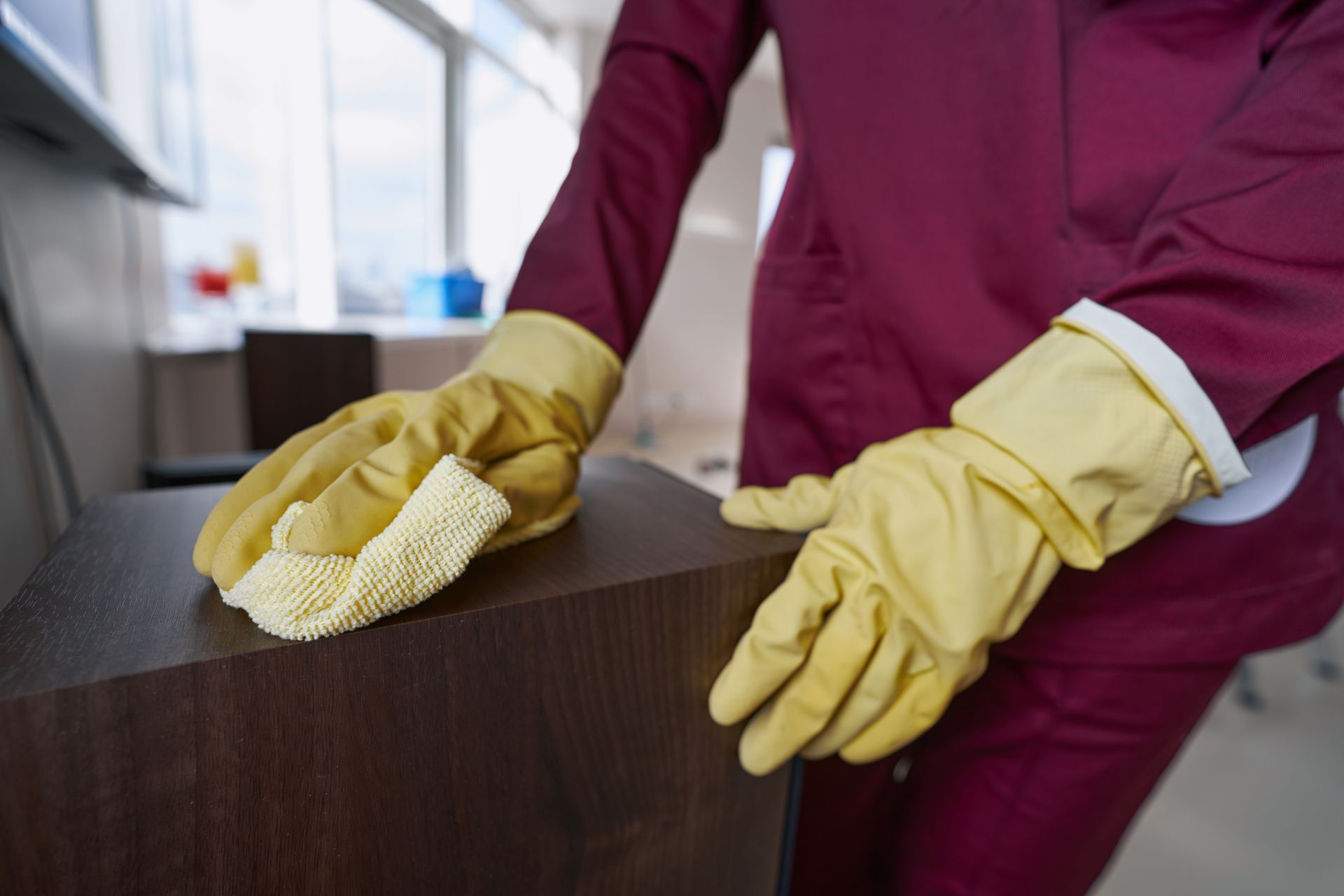 Gloved hands wiping down a wooden surface during routine cleaning and sanitizing.
