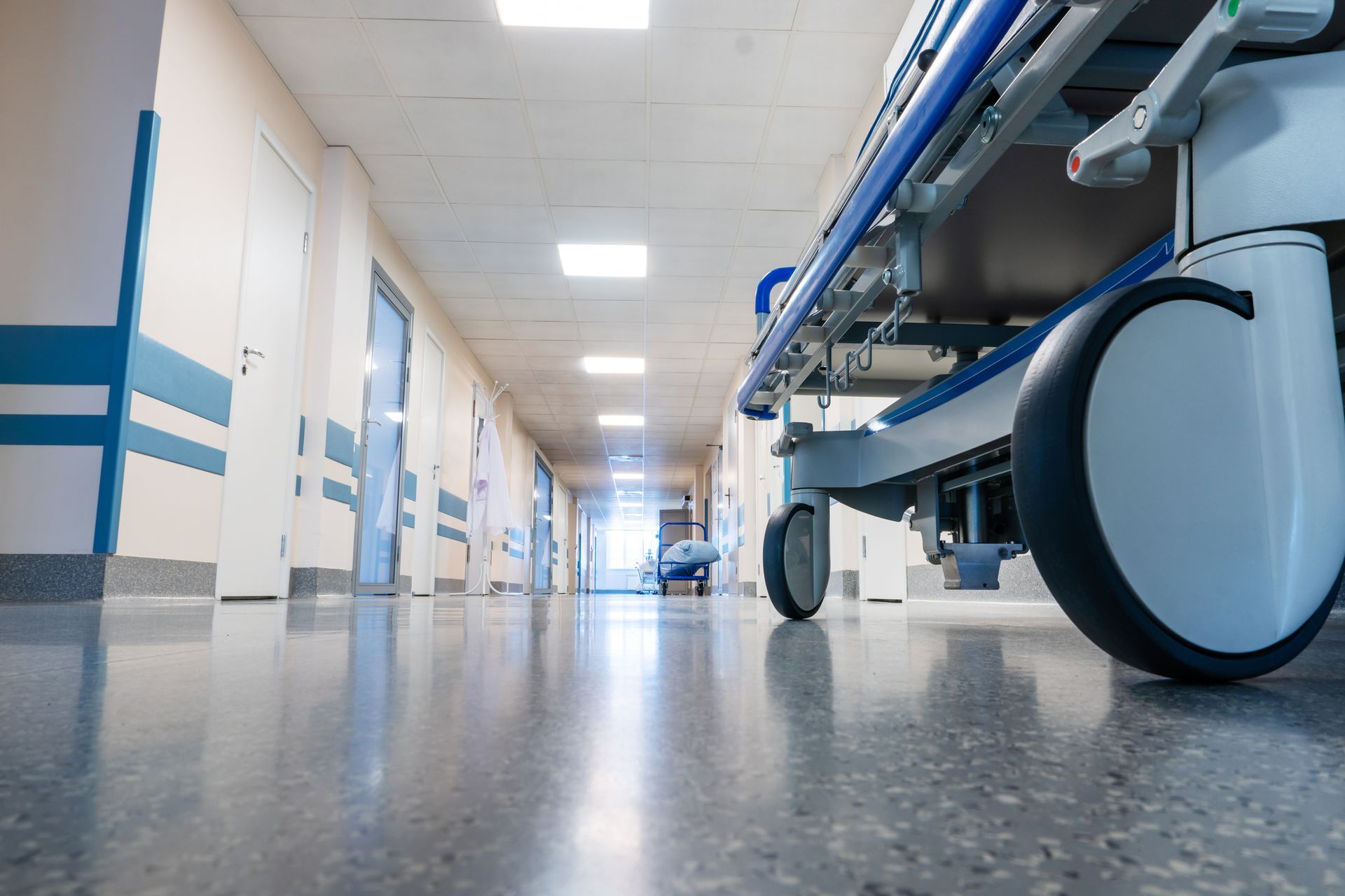 Hospital hallway with a gurney; shiny floor, doors line the sides.