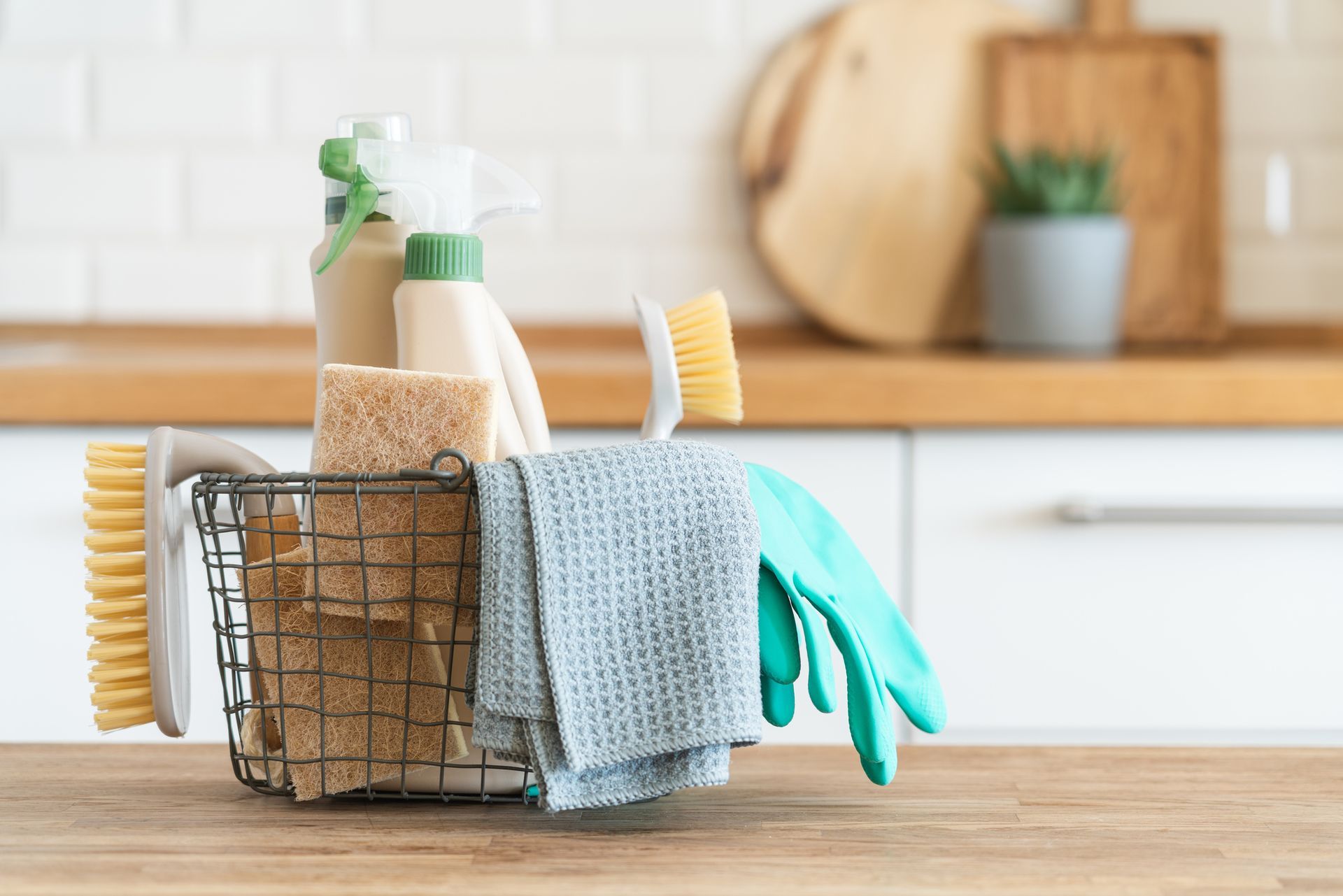 Cleaning supplies in a wire basket on a wooden countertop, kitchen backdrop.
