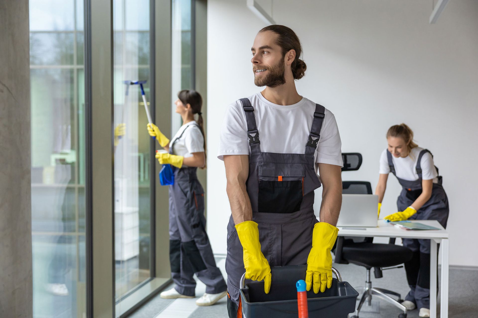 Male & female housekeeping staff performing janitorial cleaning service together in a bright lobby.
