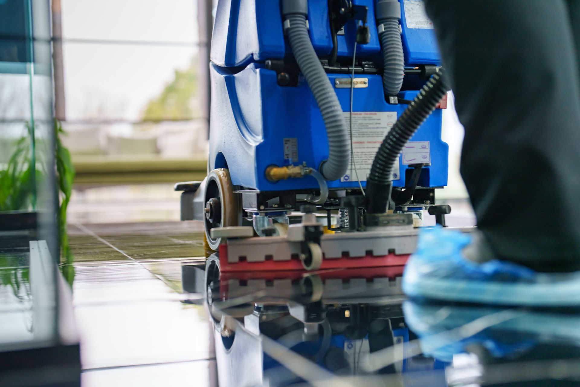 Person cleaning a glossy floor with a blue floor scrubber machine, wearing blue shoe covers.