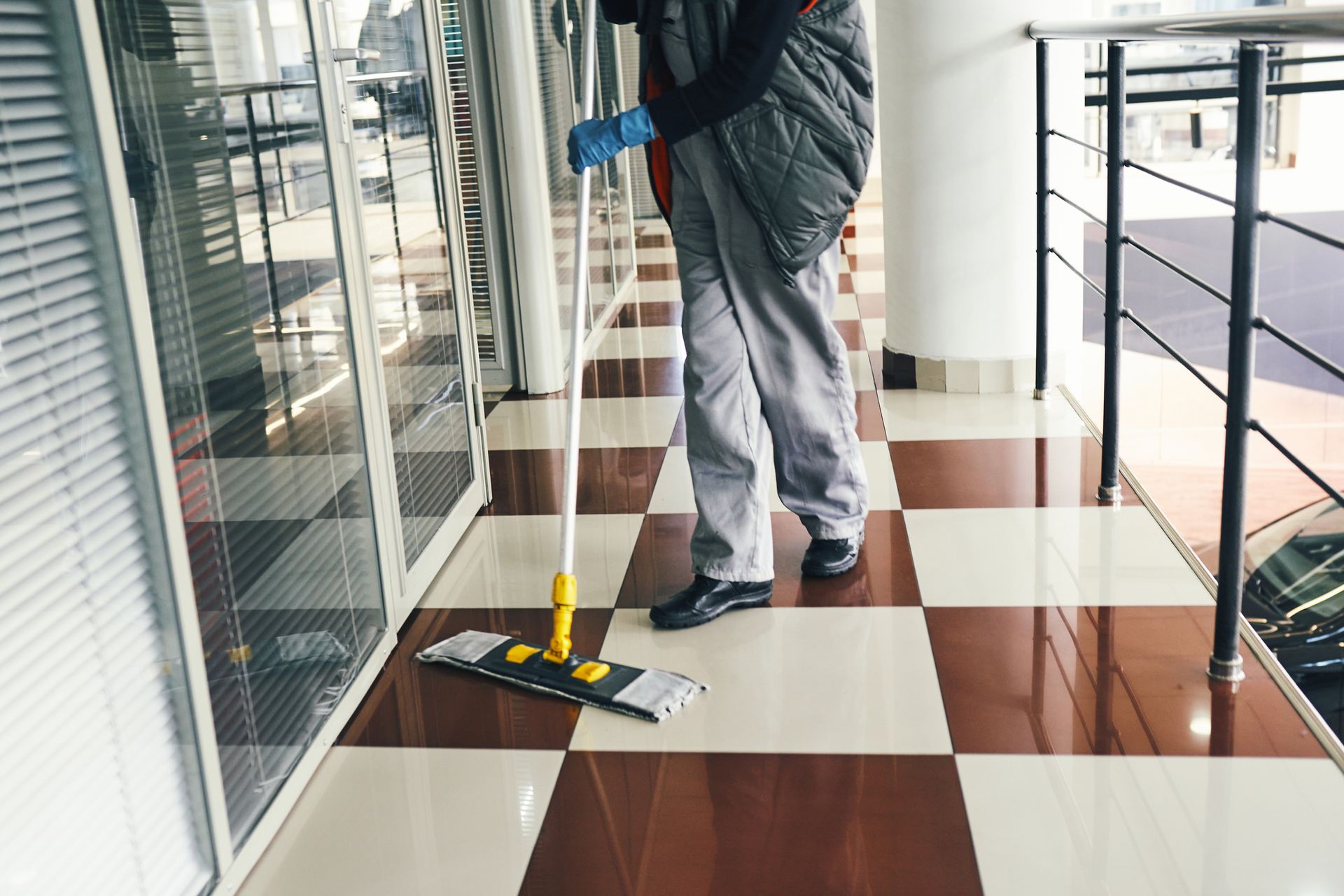 Janitorial cleaning service worker mopping tiled office hallway with professional tools.