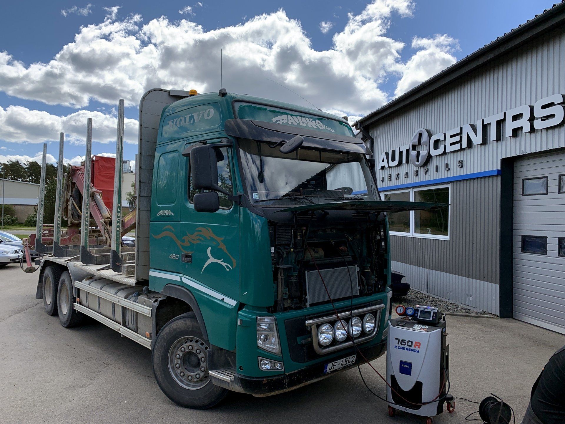 Zaļa kravas automašīna ir novietota pie ēkas.